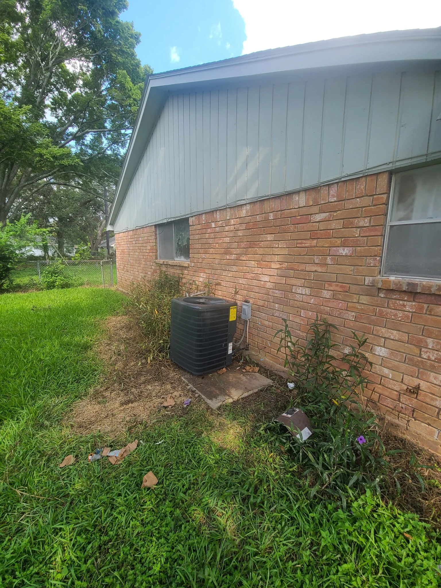 Real residential air-conditioning condenser installed beside a brick Houston-area home