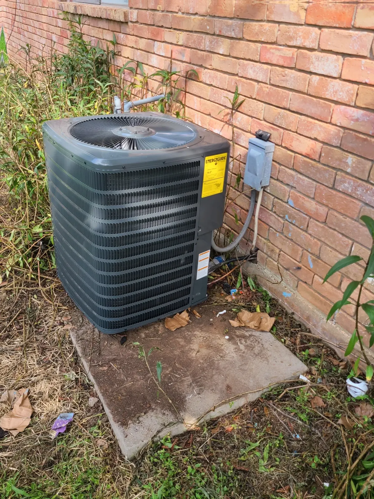 Outdoor AC condenser installed beside a brick home